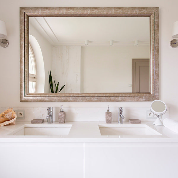 A bathroom with a white vanity and double sink, with a large mirror hanging above, in a gold frame.