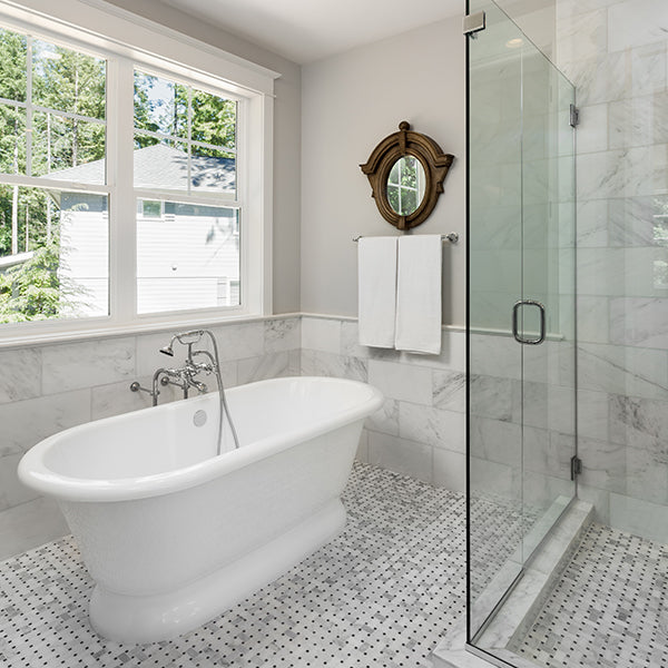 A bathroom with a large white bath tub, grey and white floor tile and a shower with glass doors.