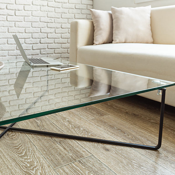 A coffee table with a glass top, in front of a beige couch on brown hardwood flooring.